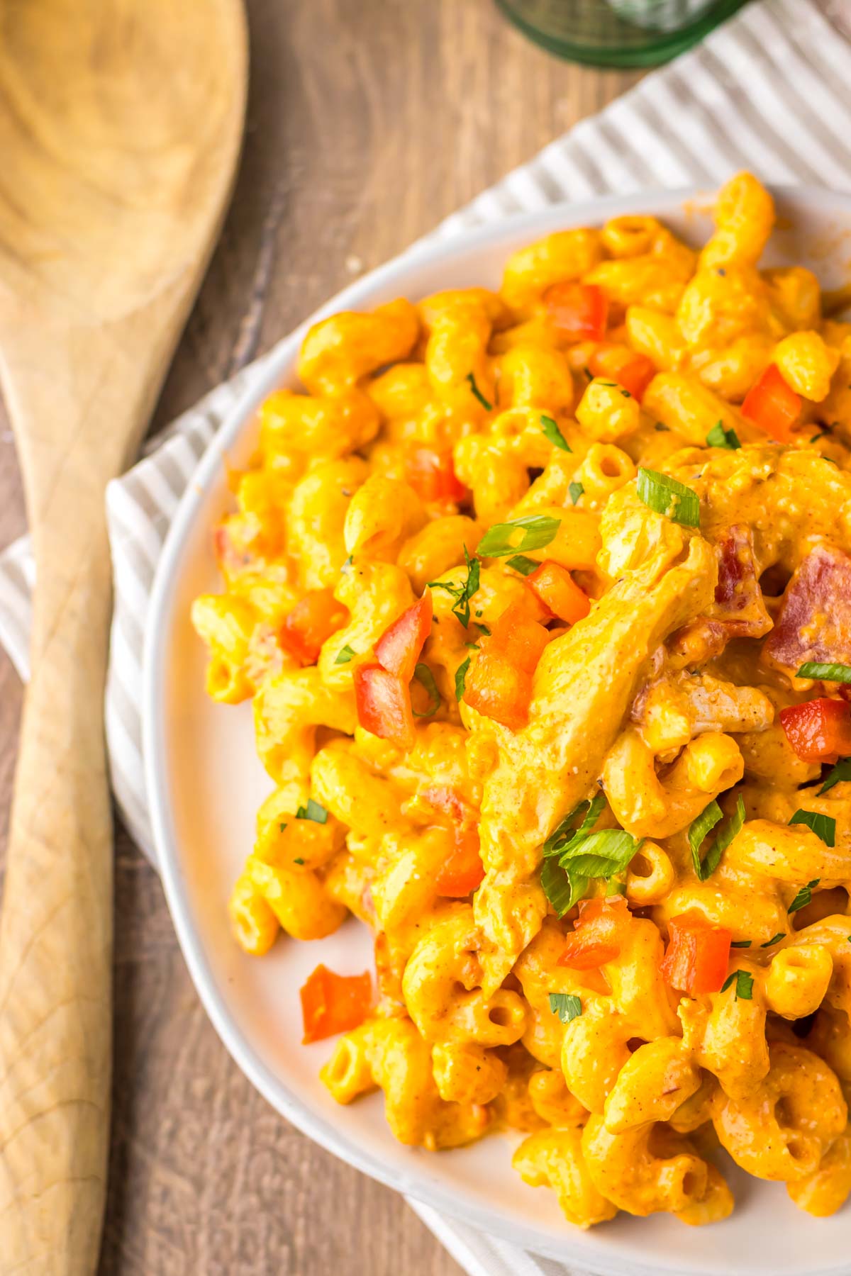 Creamy macaroni with cheese sauce, diced tomatoes, herbs, and chicken&mdash;this dish brings all the comfort of slow cooker cheesy chicken enchilada pasta, beautifully served on a white plate beside a wooden spoon.