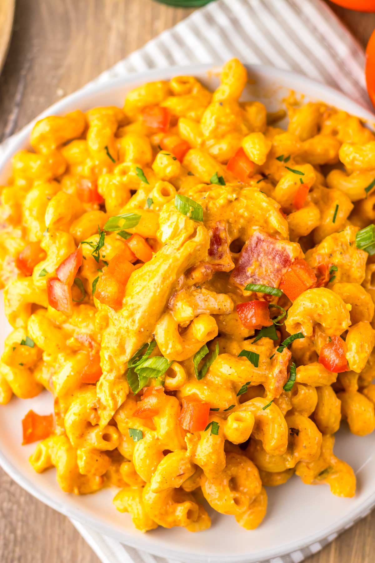 Creamy macaroni and cheese with diced tomatoes, bacon, green onions, and herbs on a white plate&mdash;reminiscent of the comforting flavors found in slow cooker cheesy chicken enchilada pasta.