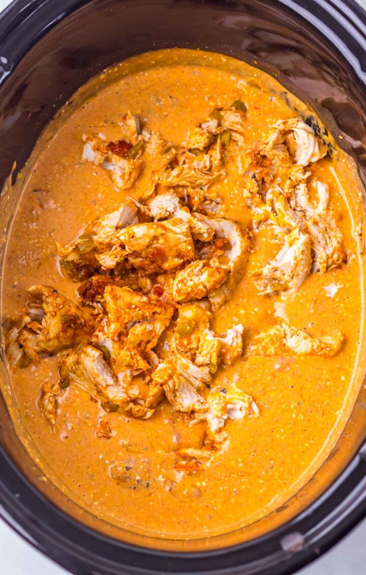Shredded chicken in a creamy orange sauce inside a black slow cooker&mdash;perfect for making delicious slow cooker cheesy chicken enchilada pasta.