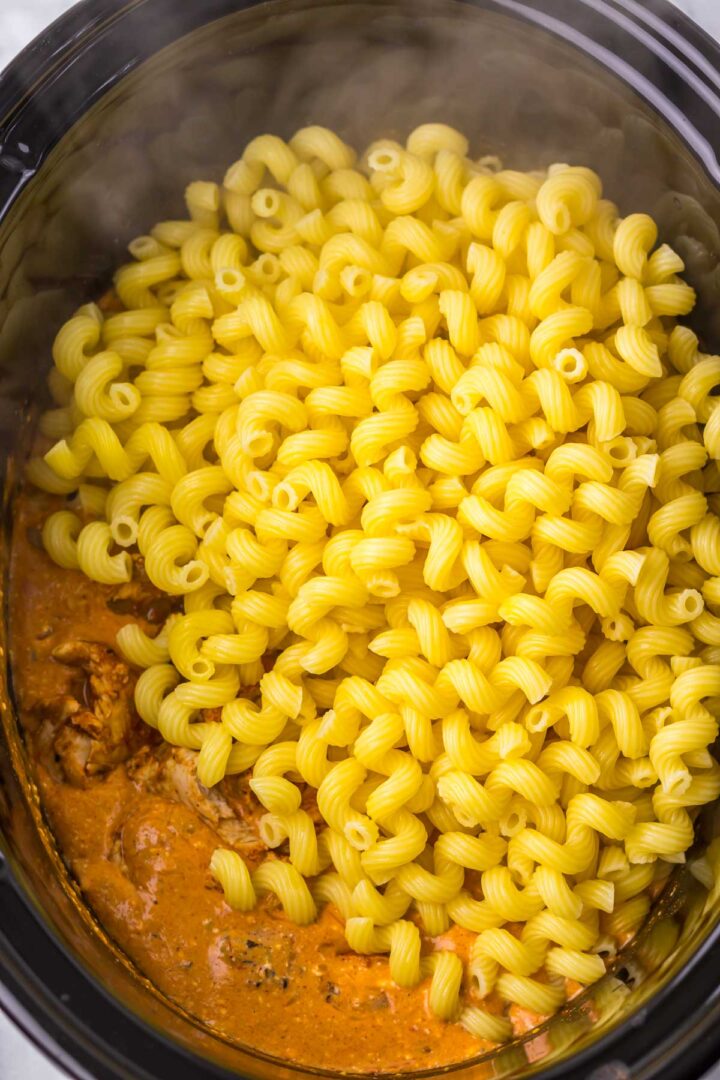 Cooked spiral pasta sits on top of creamy tomato sauce with tender chicken, creating a delicious slow cooker cheesy chicken enchilada pasta dish.