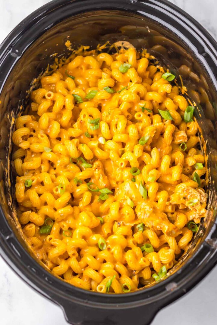 Slow cooker cheesy chicken enchilada pasta made with cavatappi, melted cheese, and chopped green onions in a black slow cooker.