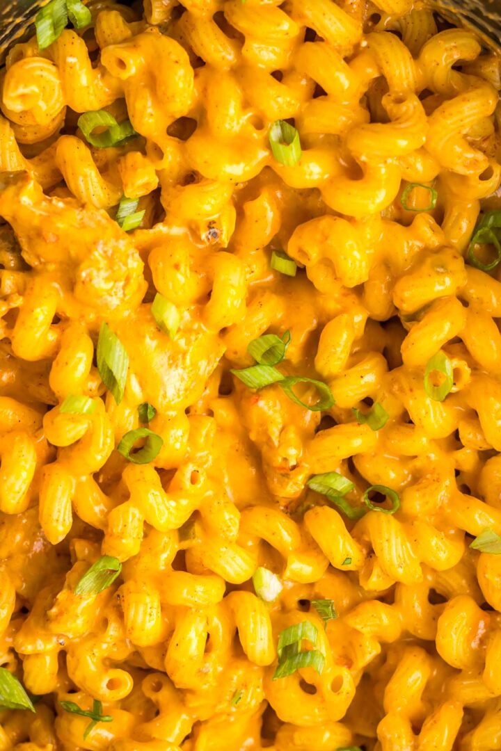 Close-up of creamy macaroni and cheese topped with chopped green onions, inspired by the flavors of slow cooker cheesy chicken enchilada pasta.
