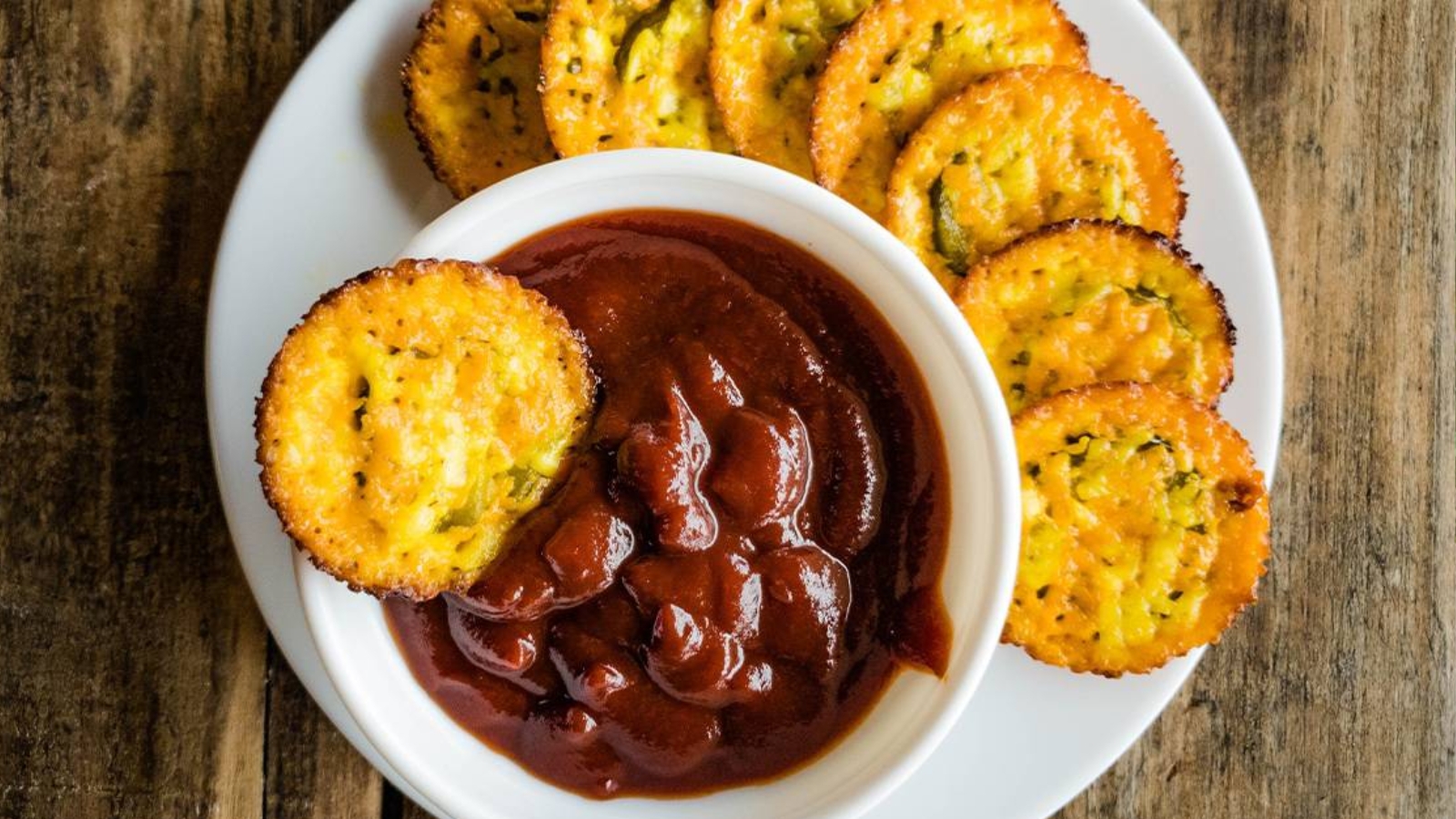 Baked pickle cheese chips with bowl of ketchup on white plate.