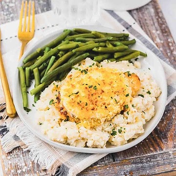 Copycat Longhorn Parmesan crusted chicken served with mashed potatoes and green beans topped with herbs.