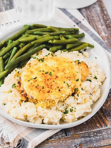 Copycat Longhorn Parmesan crusted chicken served with mashed potatoes and green beans topped with herbs.