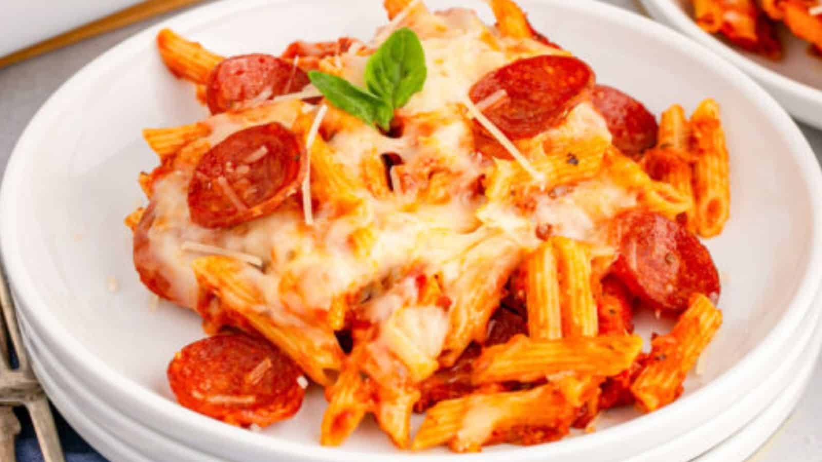 Penne pasta with tomato sauce, melted cheese, and pepperoni slices topped with fresh basil.