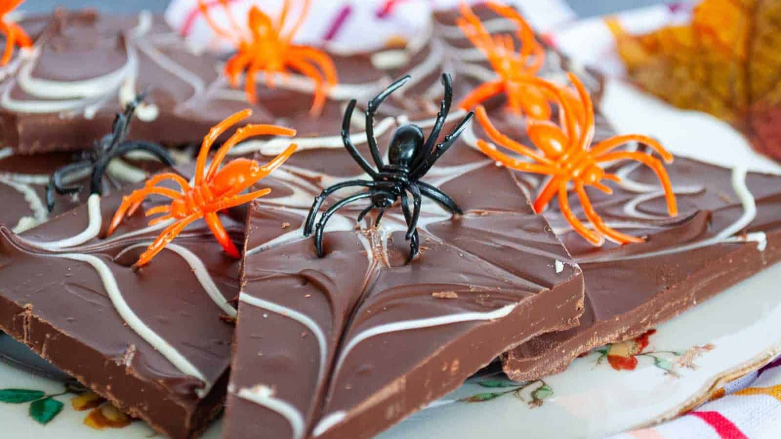 A plate of chocolate bark with spider webs and plastic spiders on it.