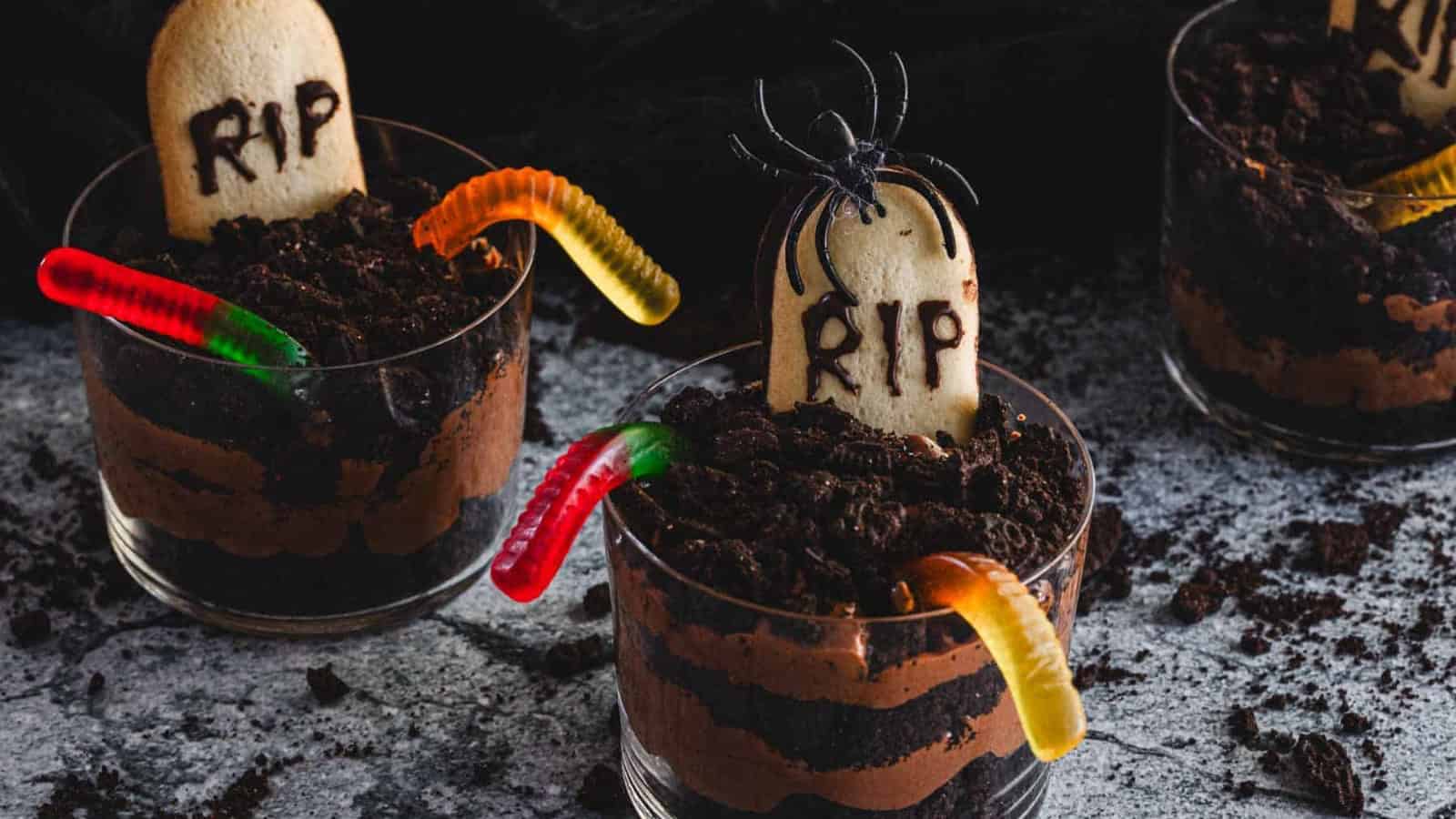 Halloween graveyard chocolate mousse cups decorated with cookie tombstones and chocolate crumbs.