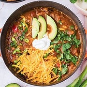 Bowl of leftover turkey pumpkin chili topped with shredded cheese, sour cream, avocado slices, and cilantro.