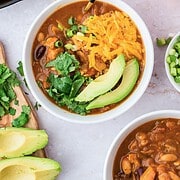 A bowl of leftover turkey pumpkin chili topped with shredded cheese, avocado, cilantro, and green onions.