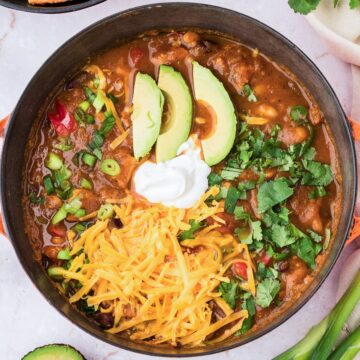 Bowl of leftover turkey pumpkin chili topped with shredded cheese, sour cream, avocado slices, and cilantro.
