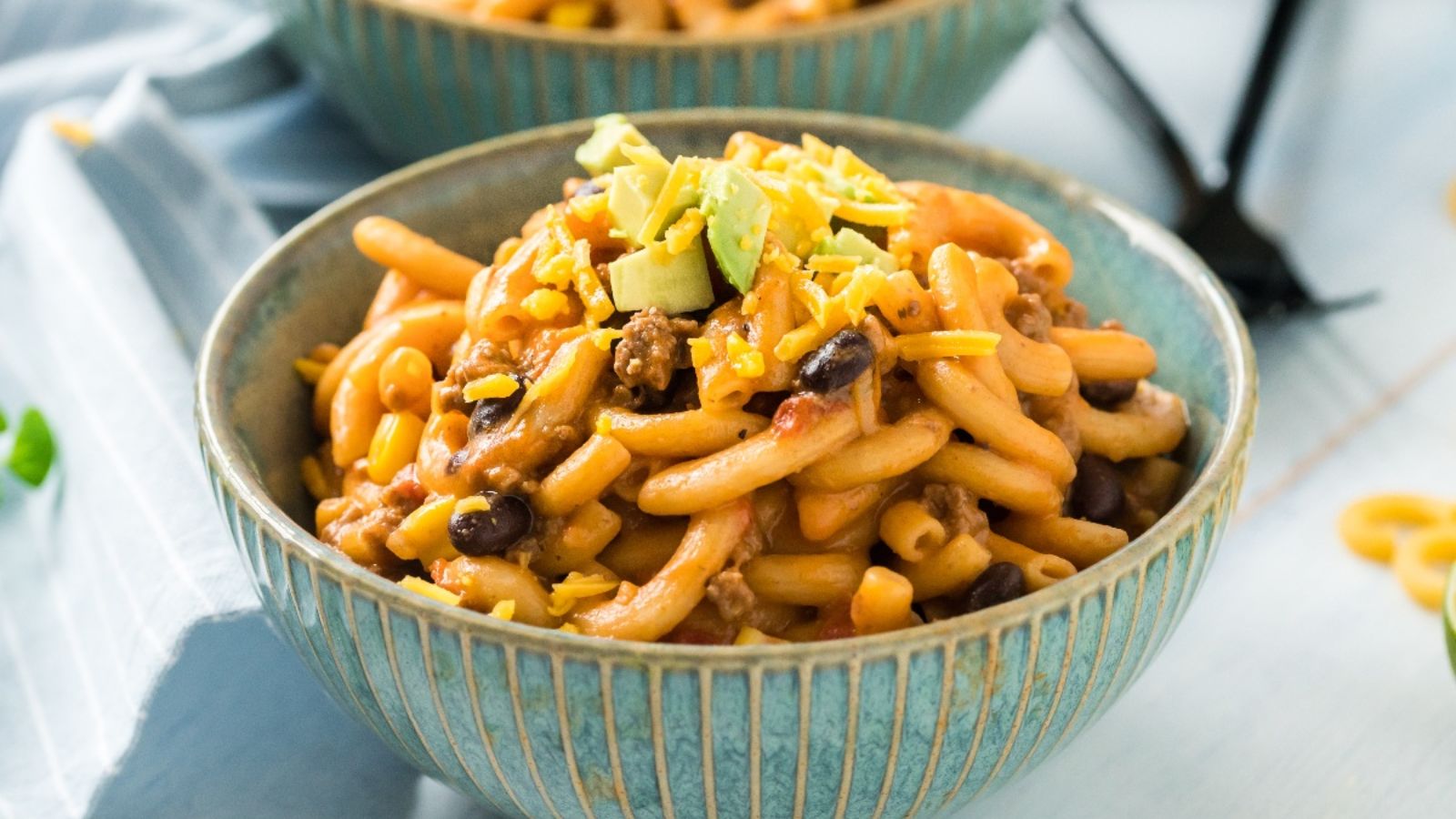 A bowl of macaroni, black beans, and ground meat topped with shredded cheese and avocado.