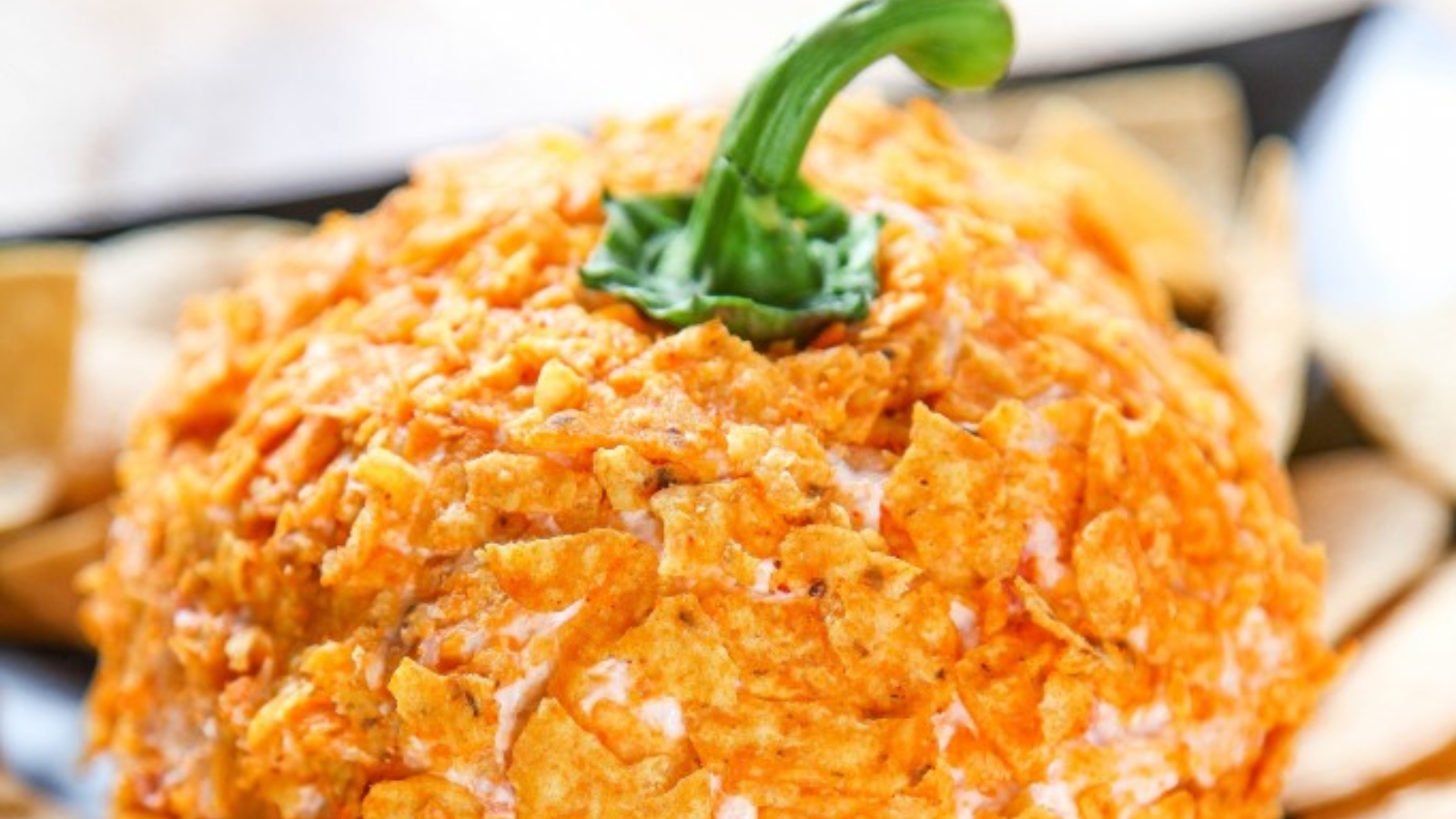 A dorito pumpkin cheeseball topped with a bell pepper stem surrounded by chips.
