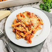 A serving of cheesy sausage pasta bake with meat sauce on a white plate.