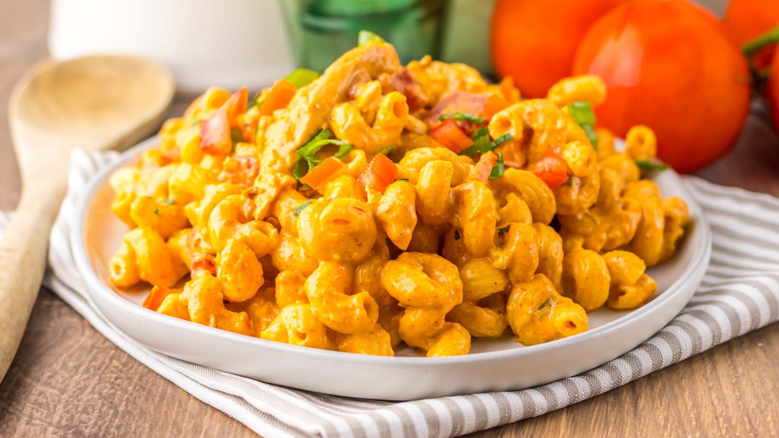 Creamy macaroni pasta with diced vegetables and herbs served on a white plate, striped napkin underneath.