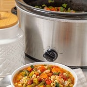 A bowl of Slow Cooker Minestrone Soup in front of the appliance.
