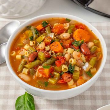 A white bowl of Slow Cooker Minestrone Soup with vegetables, beans, and pasta.