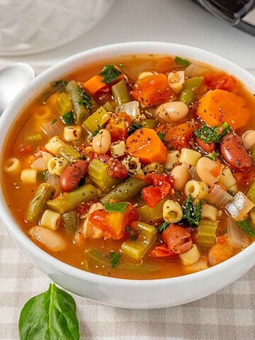 A white bowl of Slow Cooker Minestrone Soup with vegetables, beans, and pasta.