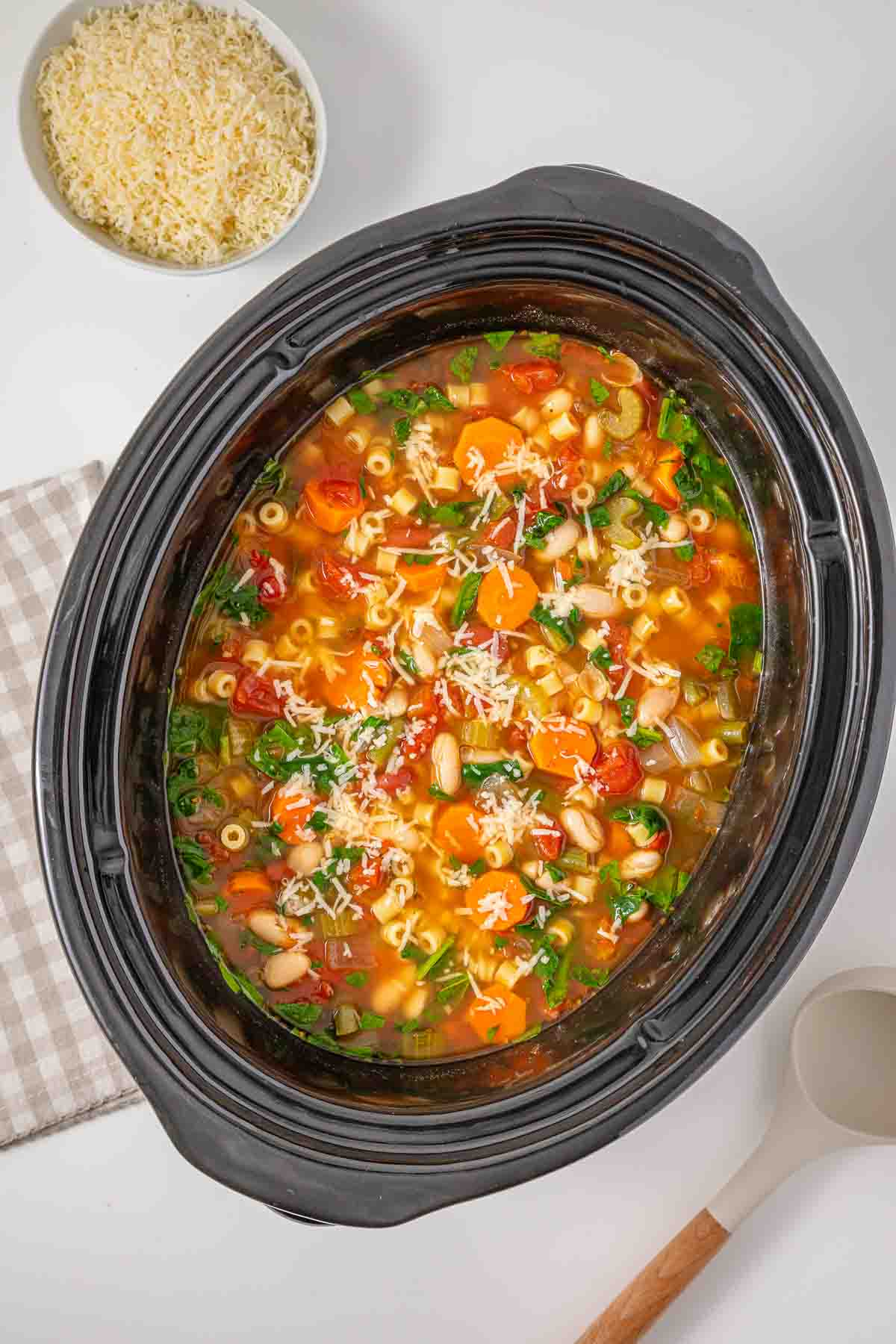 Slow cooker minestrone soup filled with pasta e fagioli, topped with shredded cheese and served with grated cheese.