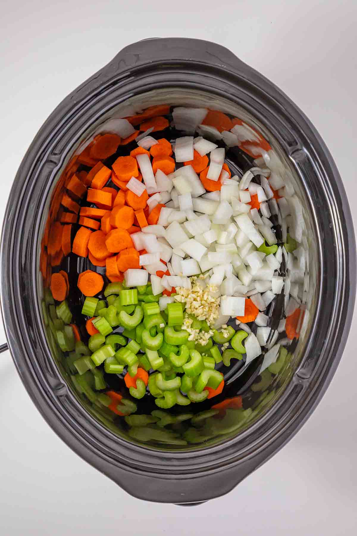 Chopped carrots, onions, celery, and minced garlic in a slow cooker for minestrone soup.