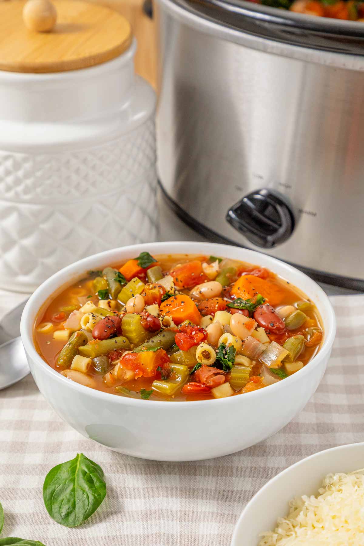 A bowl of slow cooker minestrone soup with pasta and beans, with the appliance in the background.