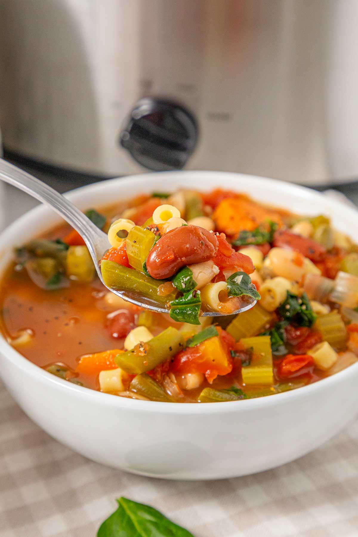 A spoonful of Slow Cooker Minestrone Soup with pasta, beans, and vegetables held over a bowl.