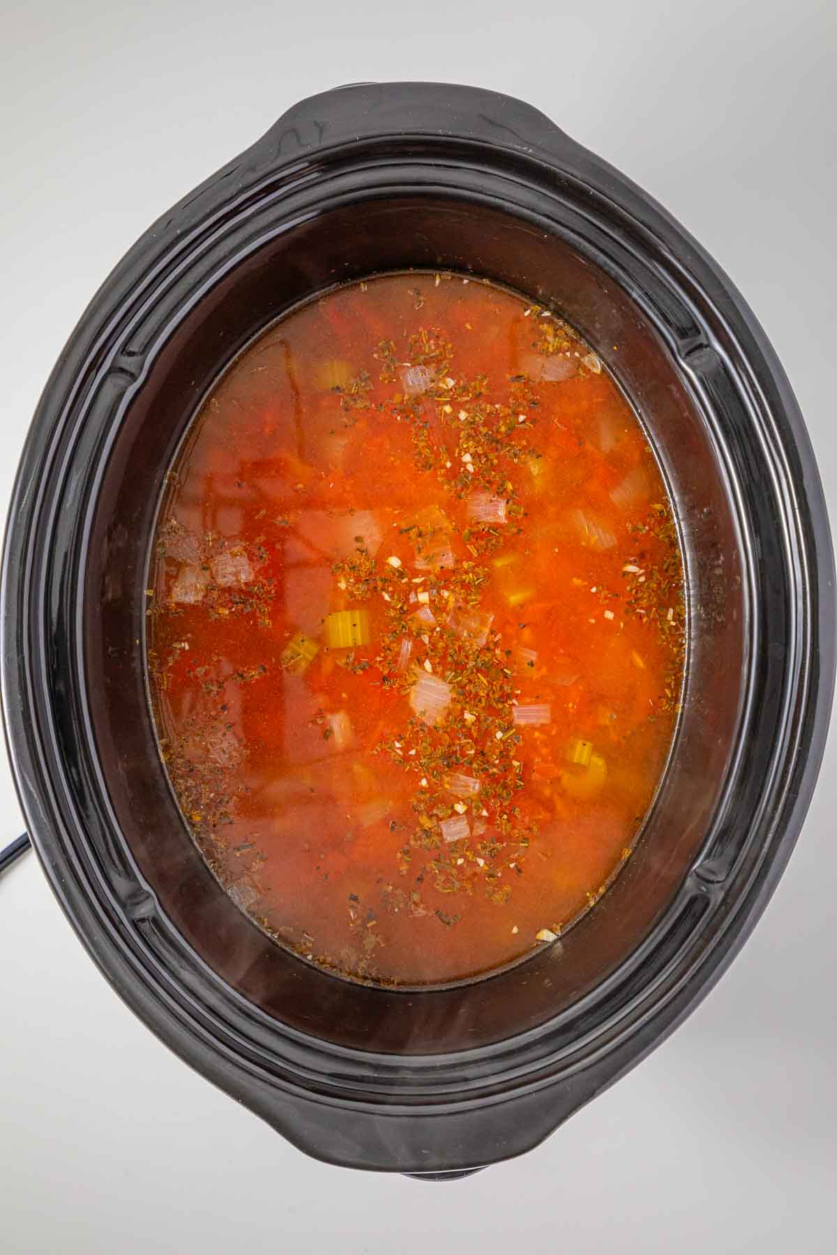 Slow cooker minestrone soup with herbs simmering in a pot.