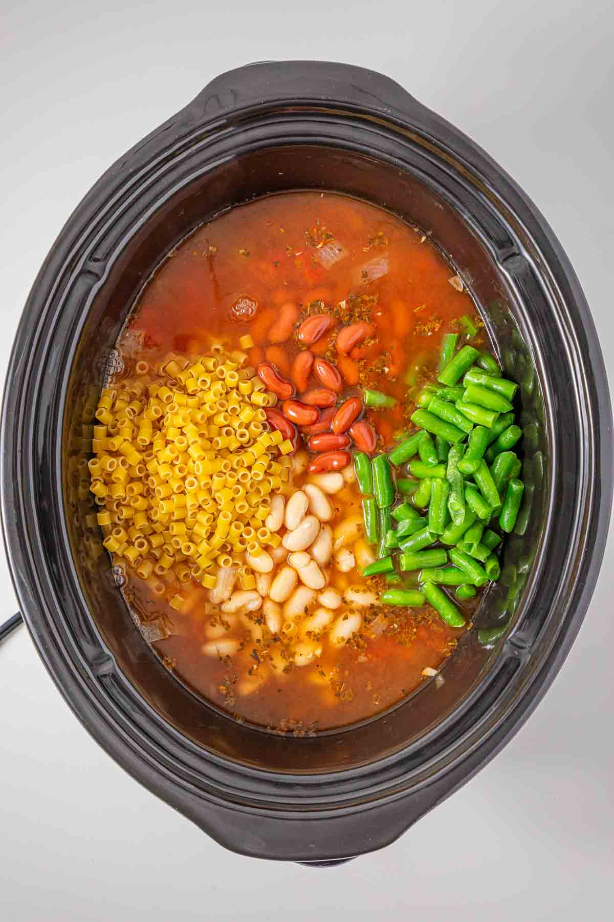 Slow cooker minestrone soup filled with broth, pasta, red beans, white beans, and green beans.