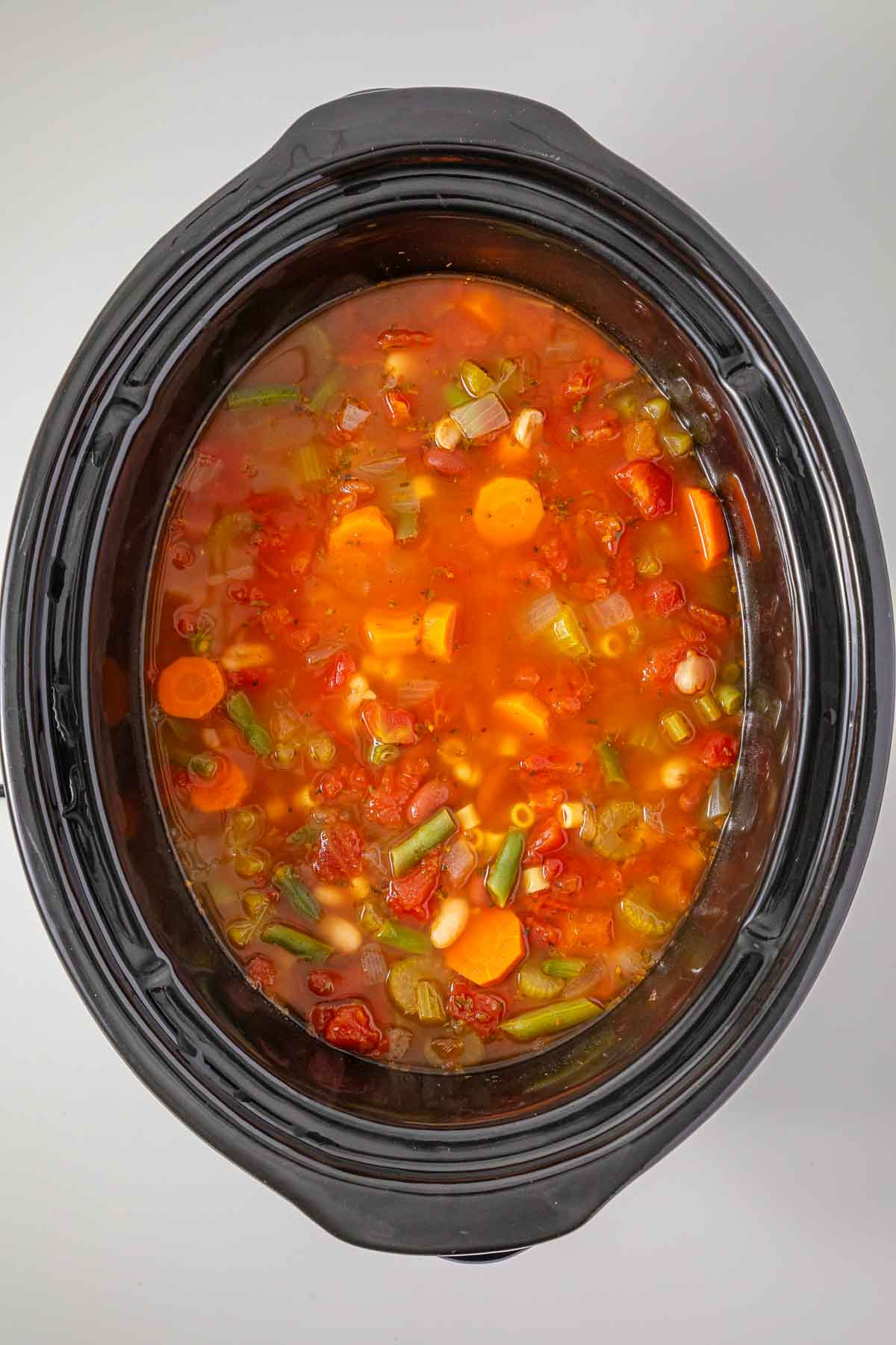 Slow Cooker Minestrone soup with beans and tomatoes simmering in the pot.