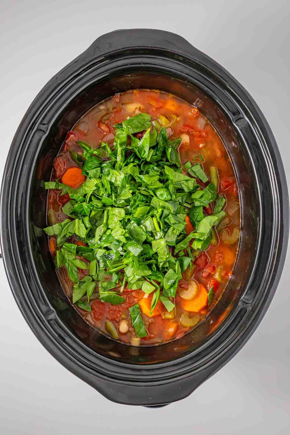 Slow cooker minestrone soup topped with chopped fresh spinach.