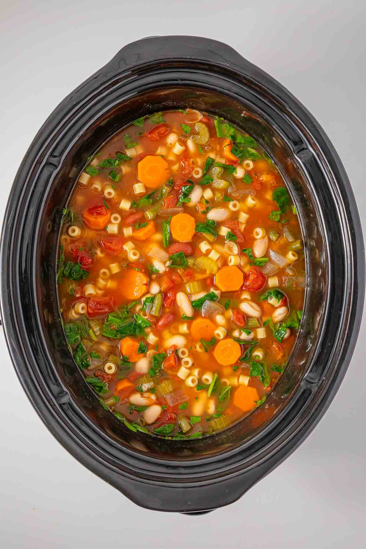 Slow cooker minestrone soup with pasta, beans, and vegetables simmering in the pot.