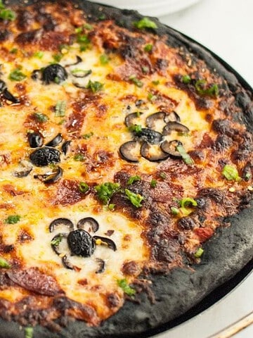 A black-crust pizza topped with cheese, pepperoni, and sliced olives arranged to look like spiders.