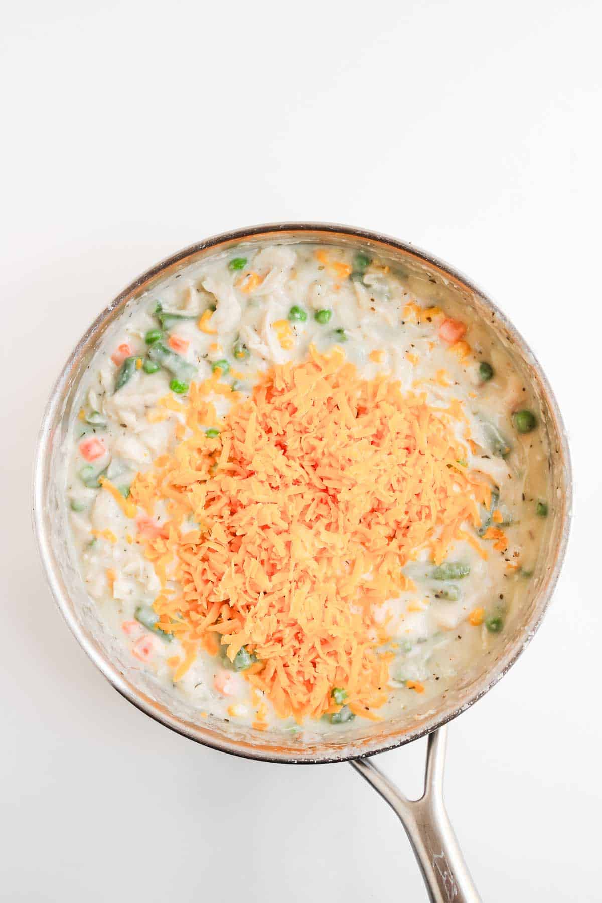 Creamy chicken pot pie with biscuits and vegetable stew in a pan, topped with shredded cheddar cheese.