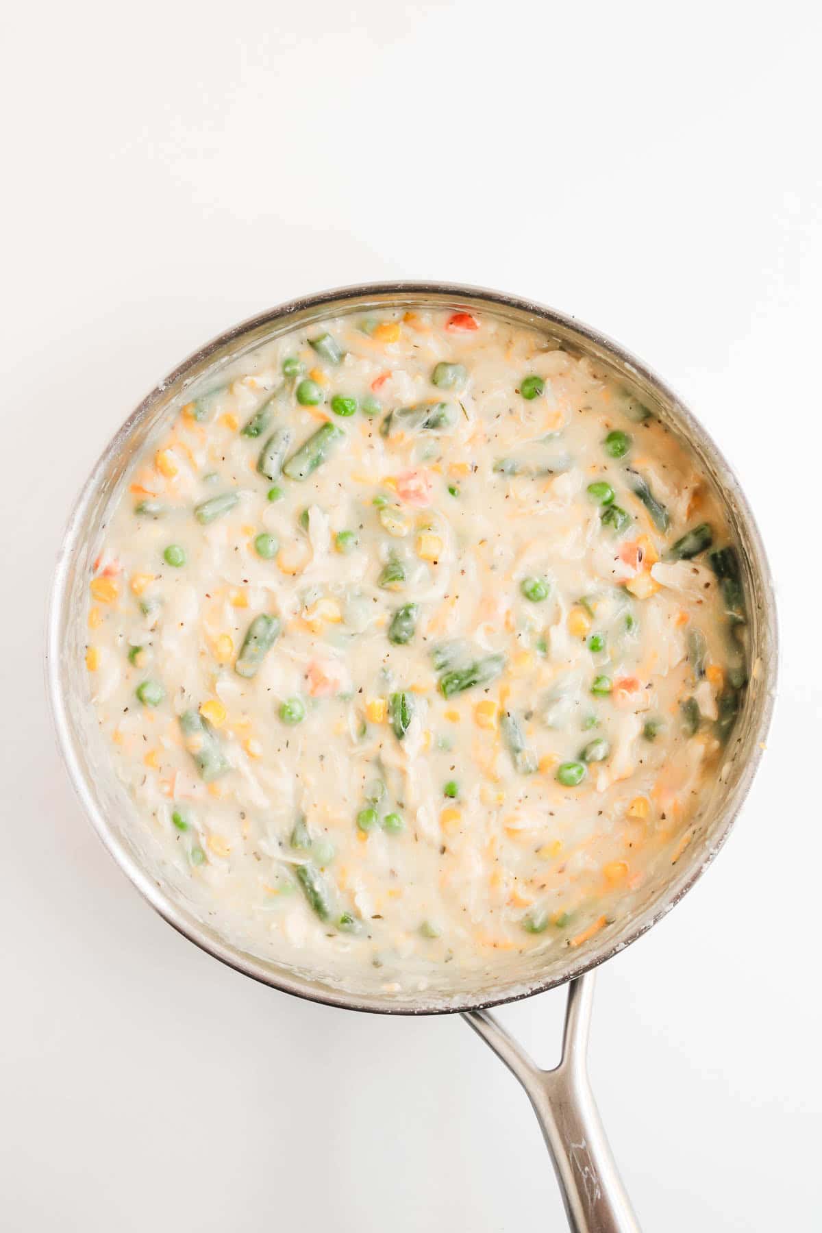 A metal saucepan filled with chicken pot pie with biscuits filling, containing vegetables and a creamy sauce.