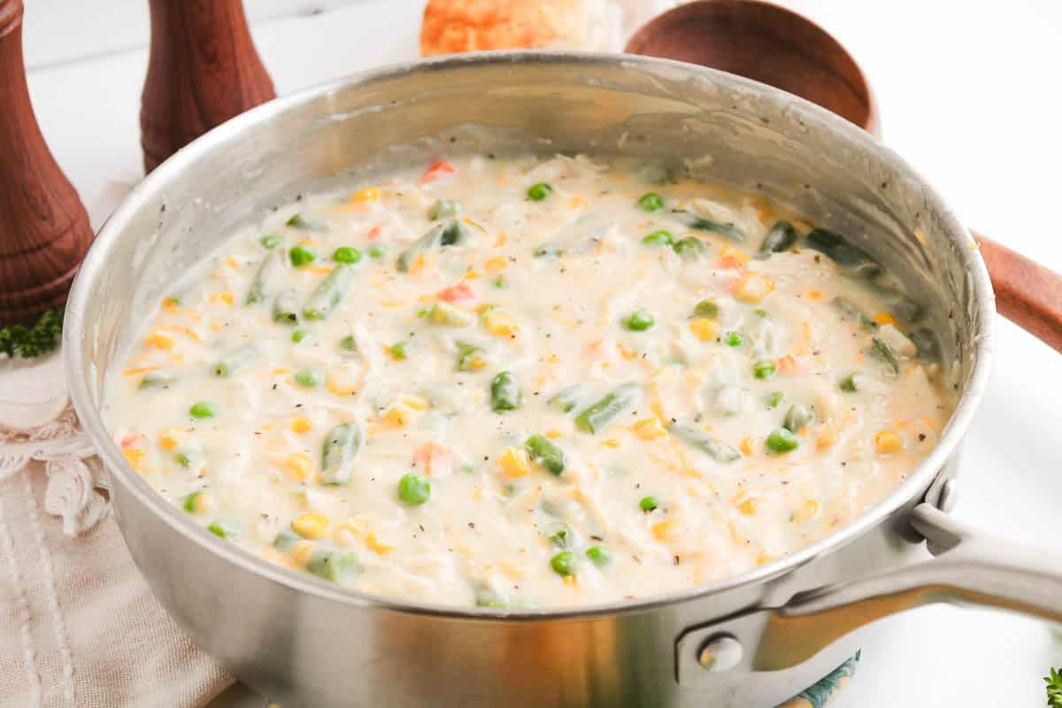 Creamy chicken pot pie stew with vegetables in a metal skillet.