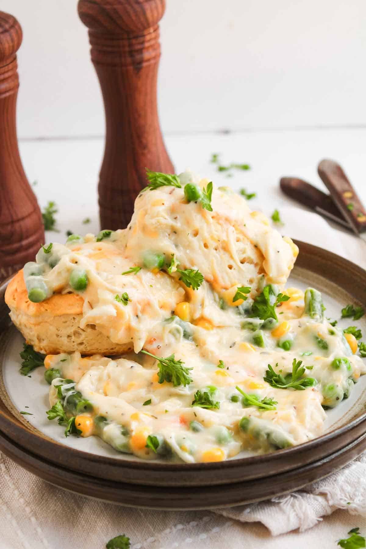 Chicken pot pie with biscuits, featuring a golden biscuit topped with creamy chicken, peas, and corn.