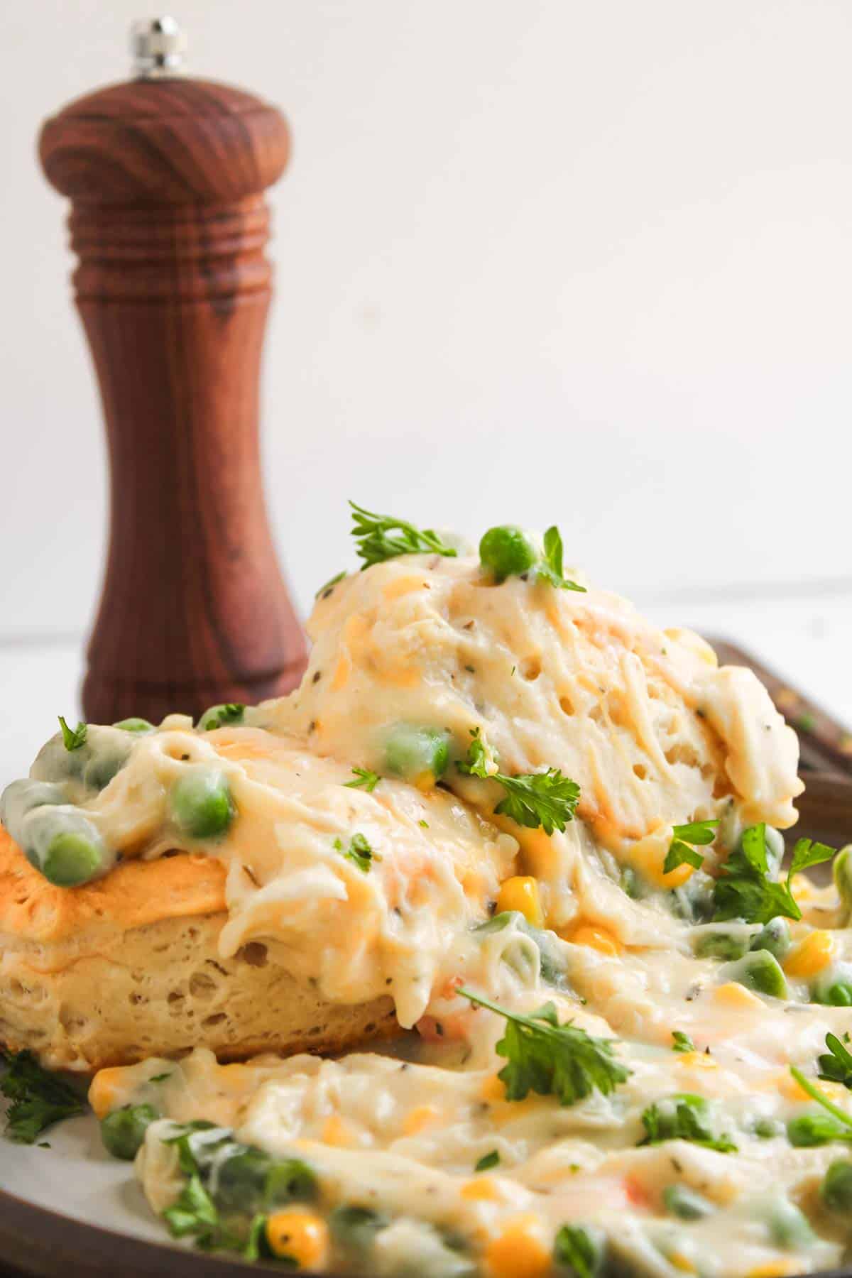 Chicken pot pie with biscuits topped with creamy chicken, peas, and corn, with a wooden pepper mill in the background.