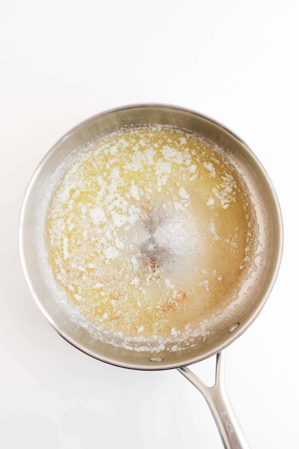 Butter melting in a stainless steel skillet for a chicken pot pie with biscuits.