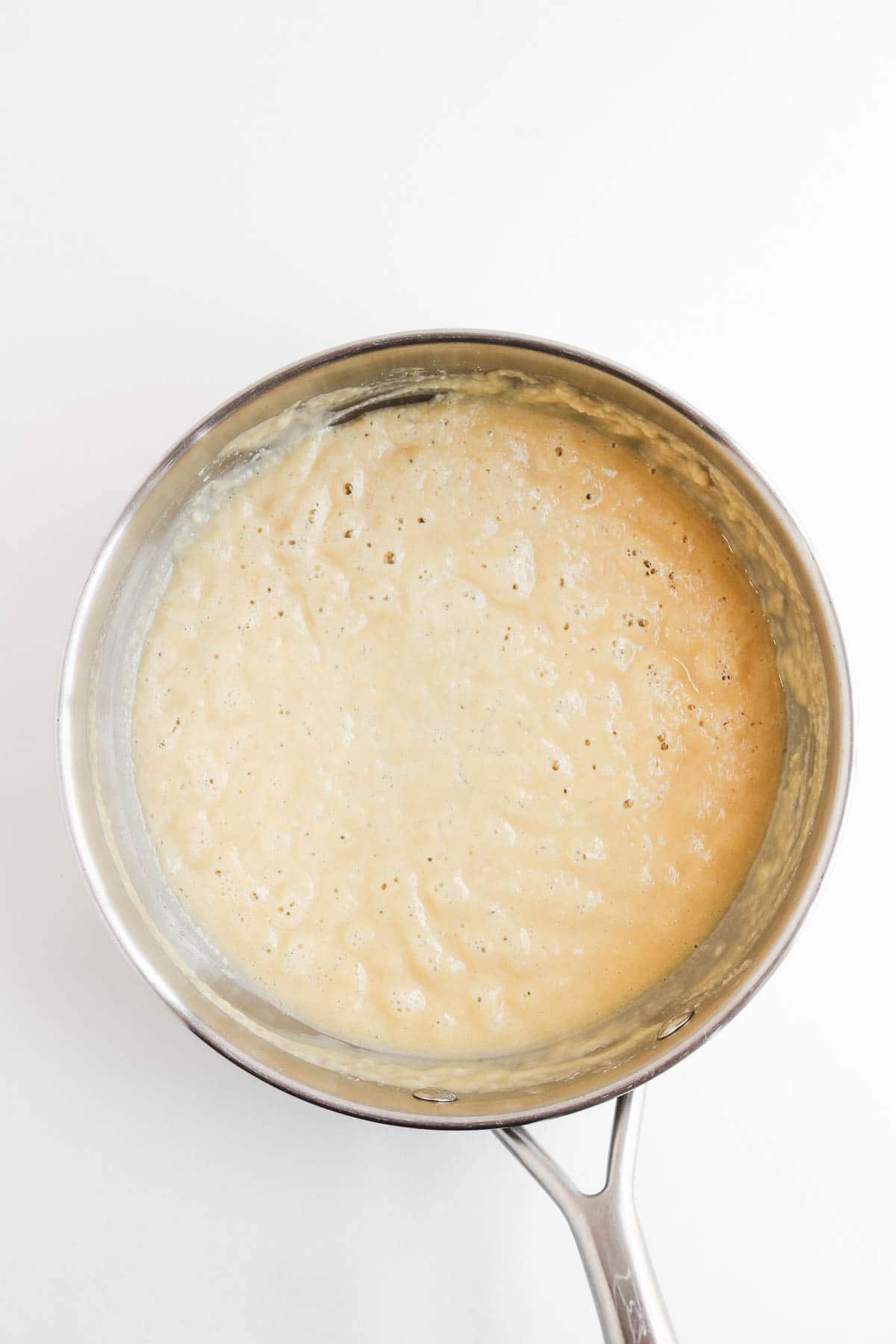 A metal saucepan containing a bubbling, beige-colored chicken pot pie sauce.