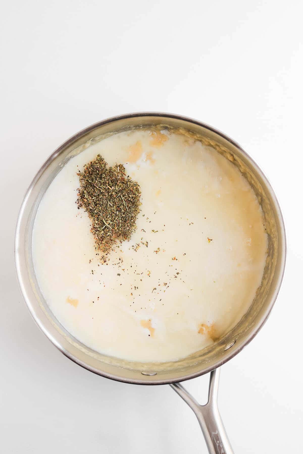 A saucepan of cream topped with dried herbs for a chicken pot pie with biscuits.