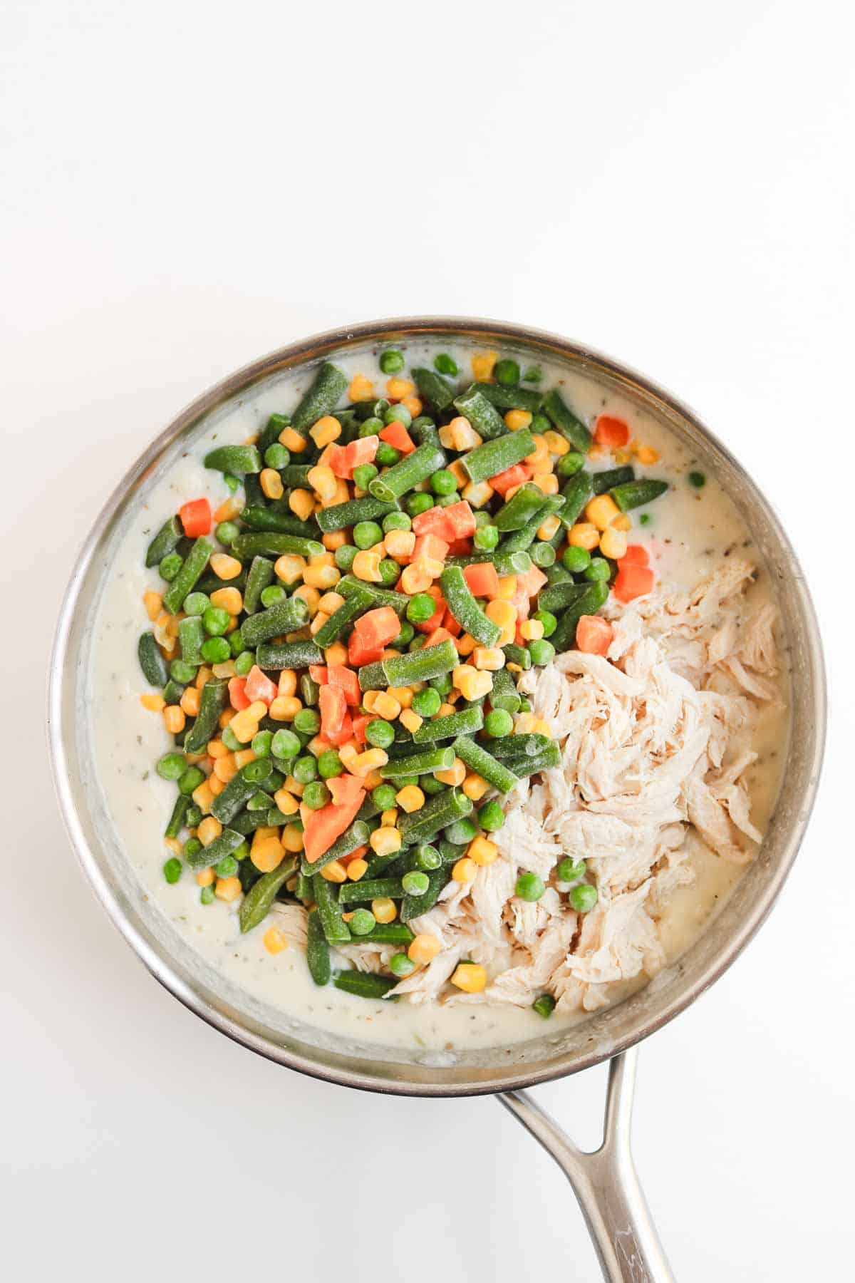 A skillet of creamy chicken pot pie filling with shredded chicken, peas, carrots, corn, and green beans.