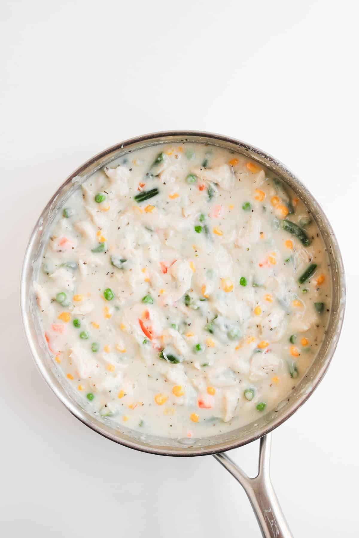 Pot of creamy chicken pot pie soup with vegetables and biscuits.