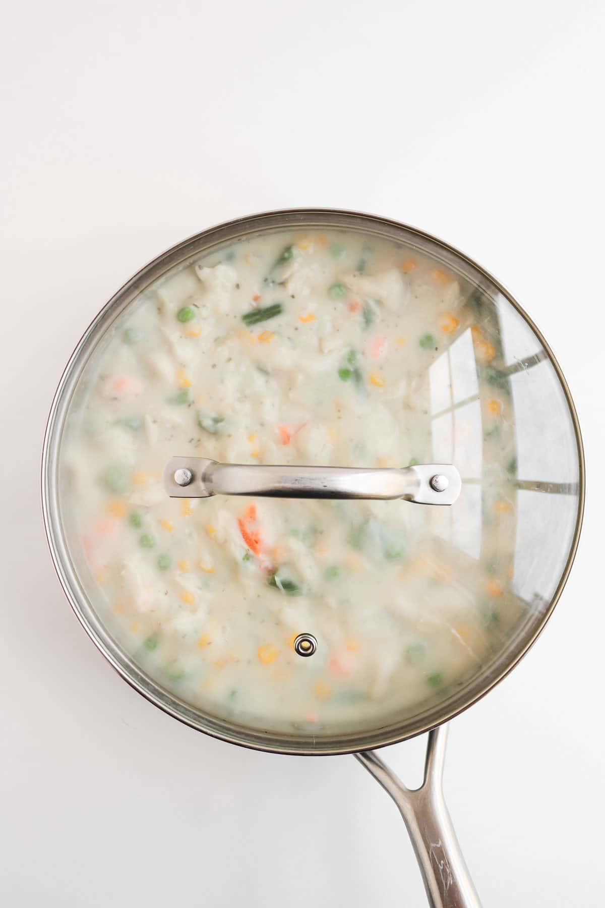 A pot of creamy chicken pot pie soup with biscuits, covered with a glass lid.