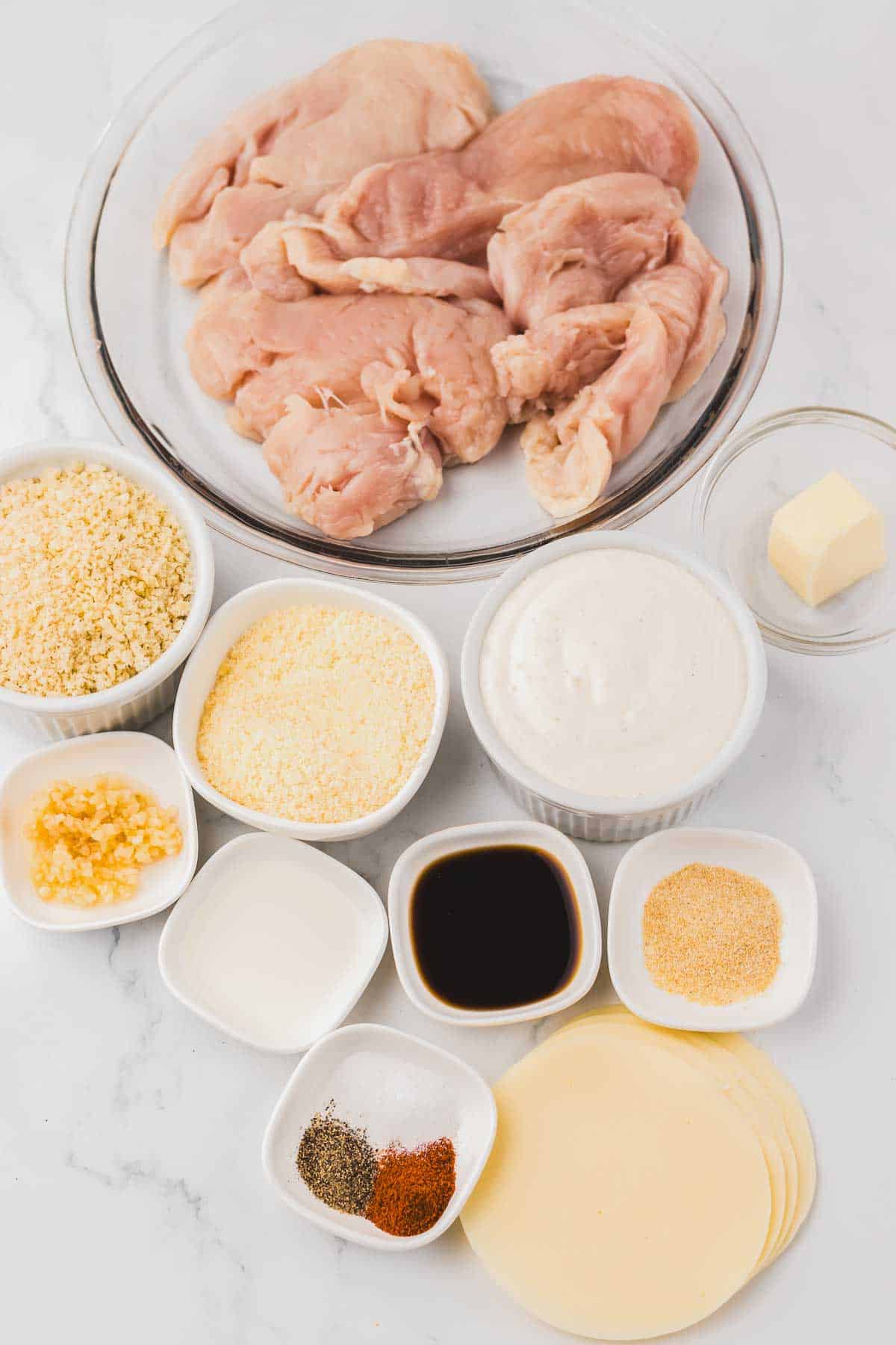 Raw chicken breast surrounded by bowls of ingredients for copycat Longhorn Parmesan crusted chicken.
