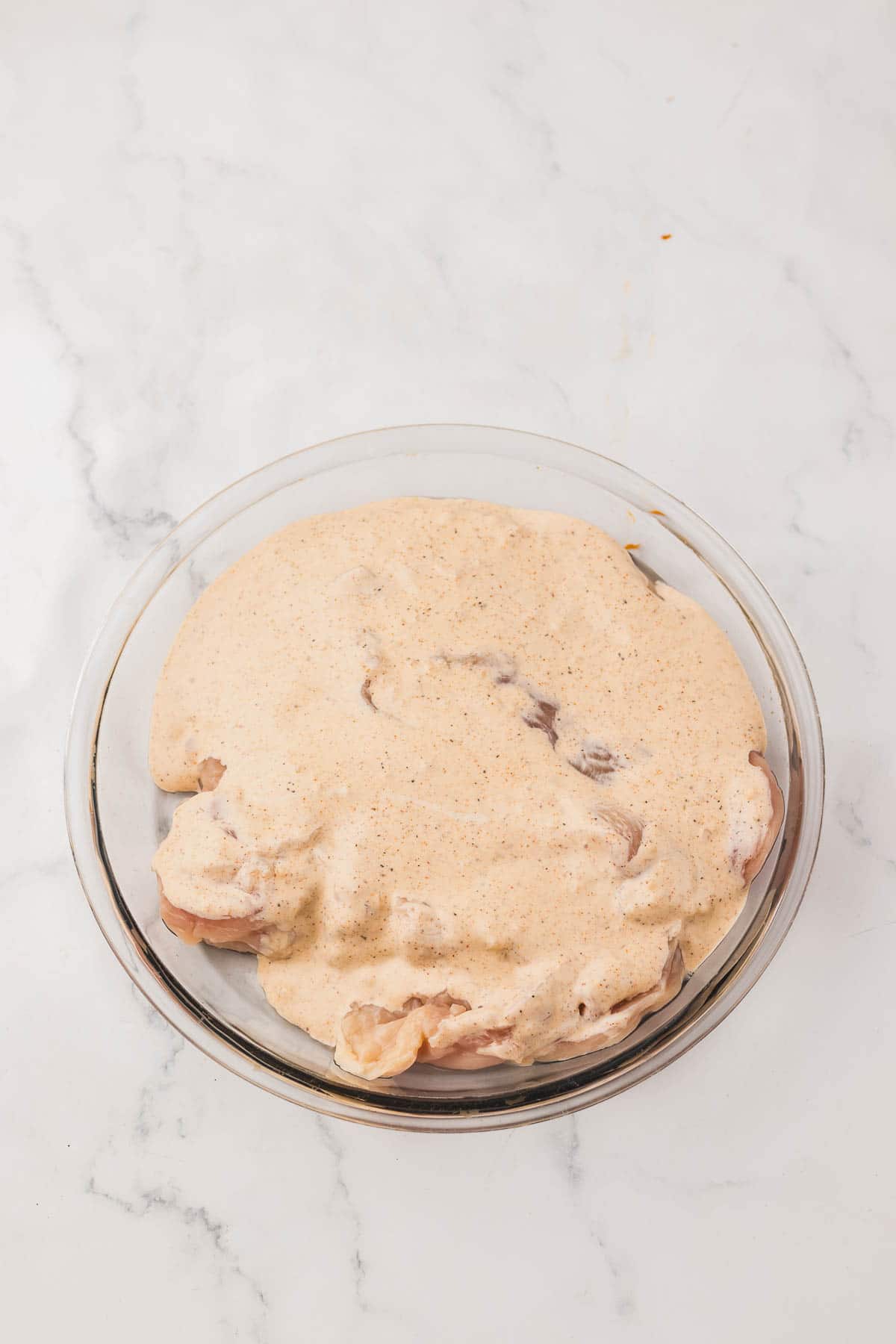 Raw chicken breasts for copycat Longhorn Parmesan crusted chicken coated in a creamy marinade in a glass bowl.