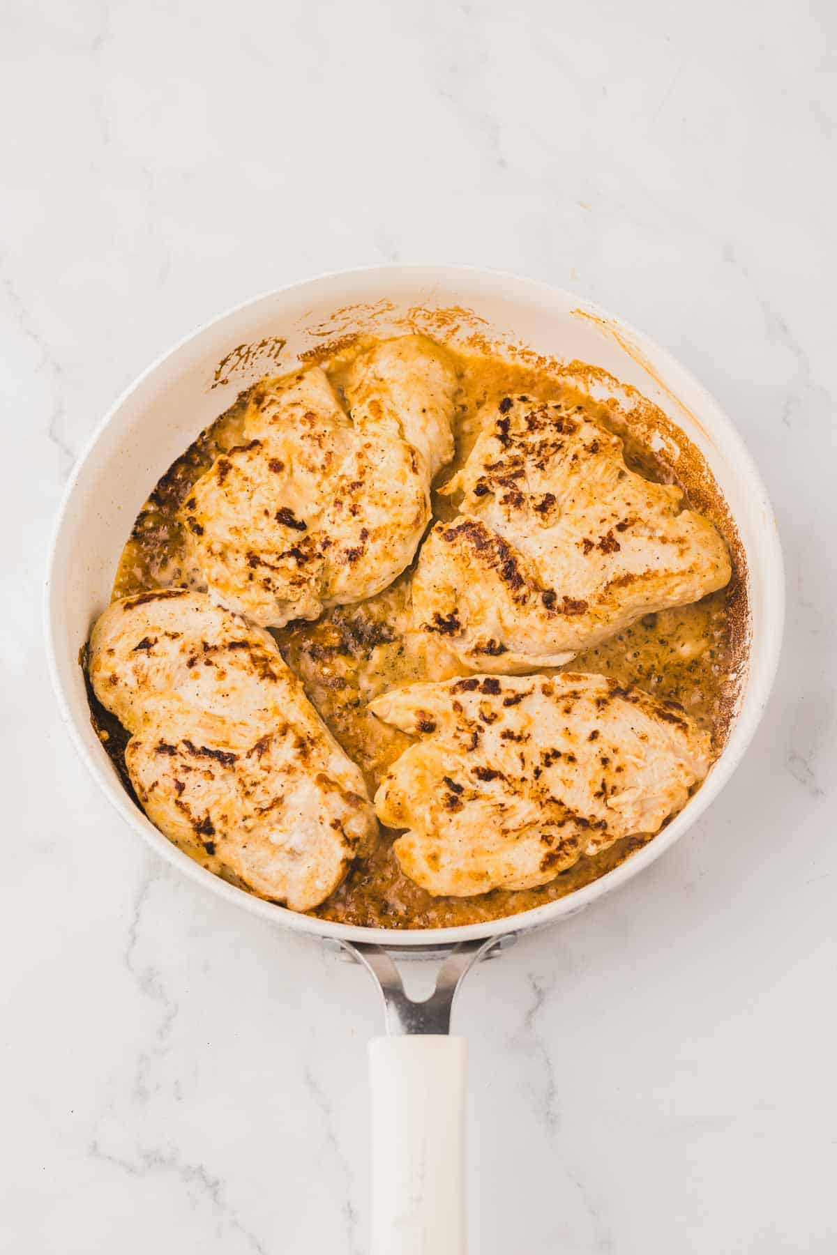 Four chicken breasts cooking in a creamy sauce in a skillet for Copycat Longhorn Parmesan Crusted Chicken.