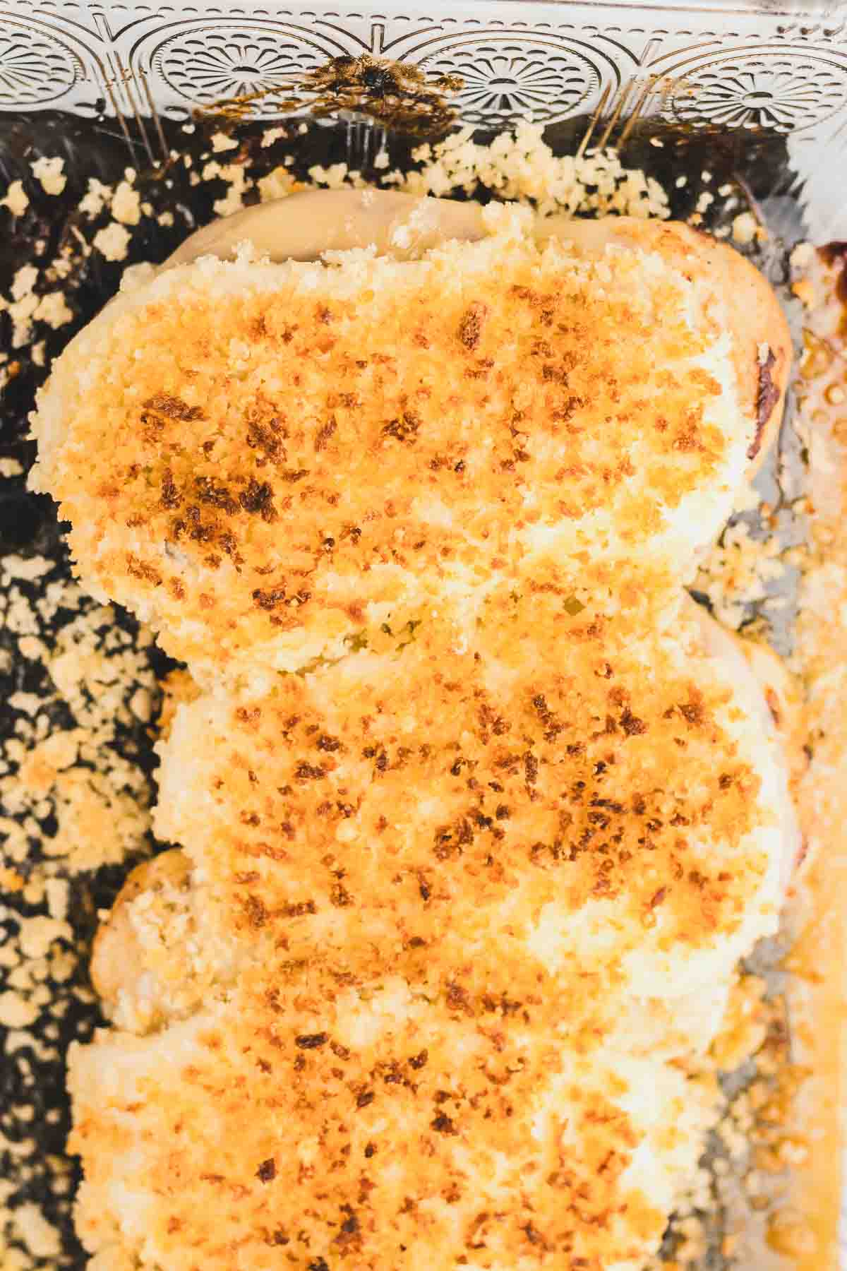 Three pieces of Copycat Longhorn Parmesan Crusted Chicken baked in a glass dish.