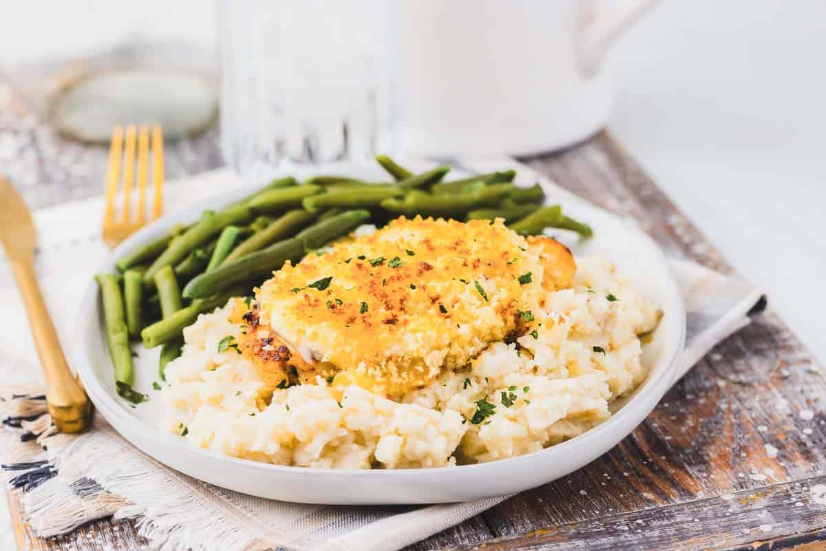 Copycat Longhorn Parmesan crusted chicken served with mashed potatoes and green beans on a white plate.