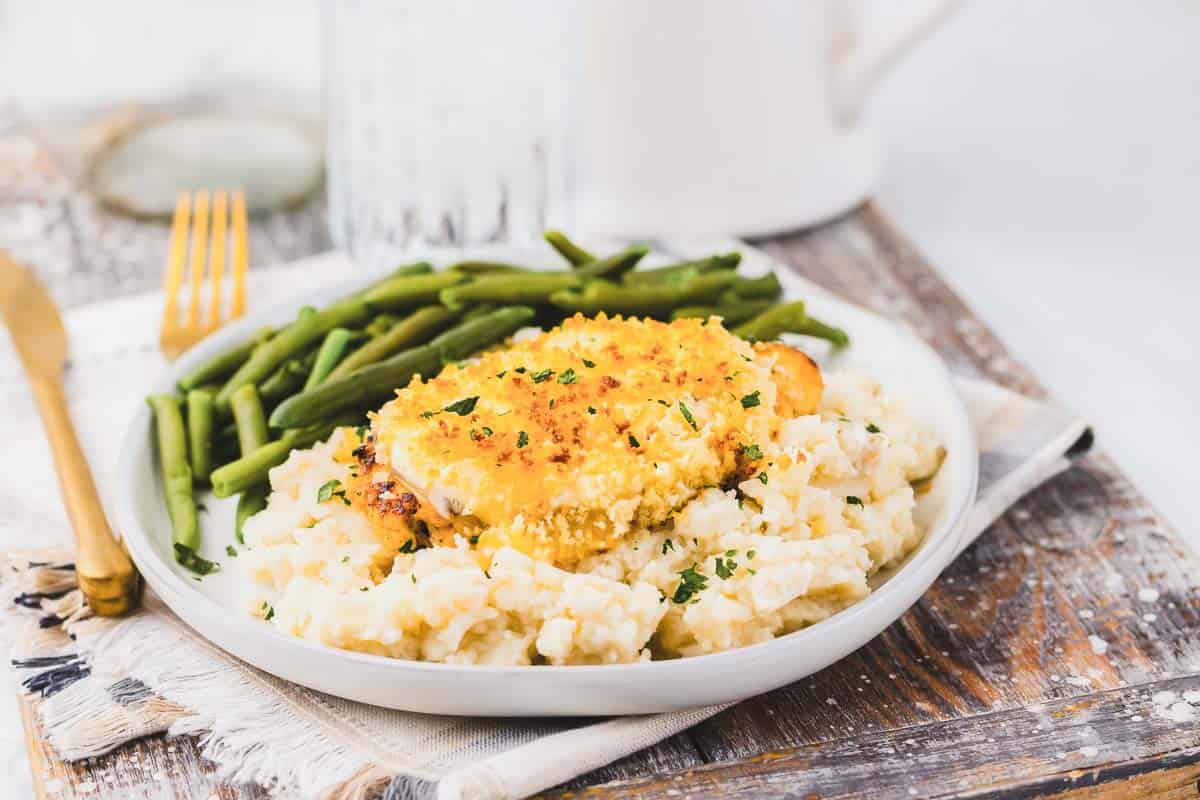 Copycat Longhorn Parmesan crusted chicken served with mashed potatoes and green beans on a plate.