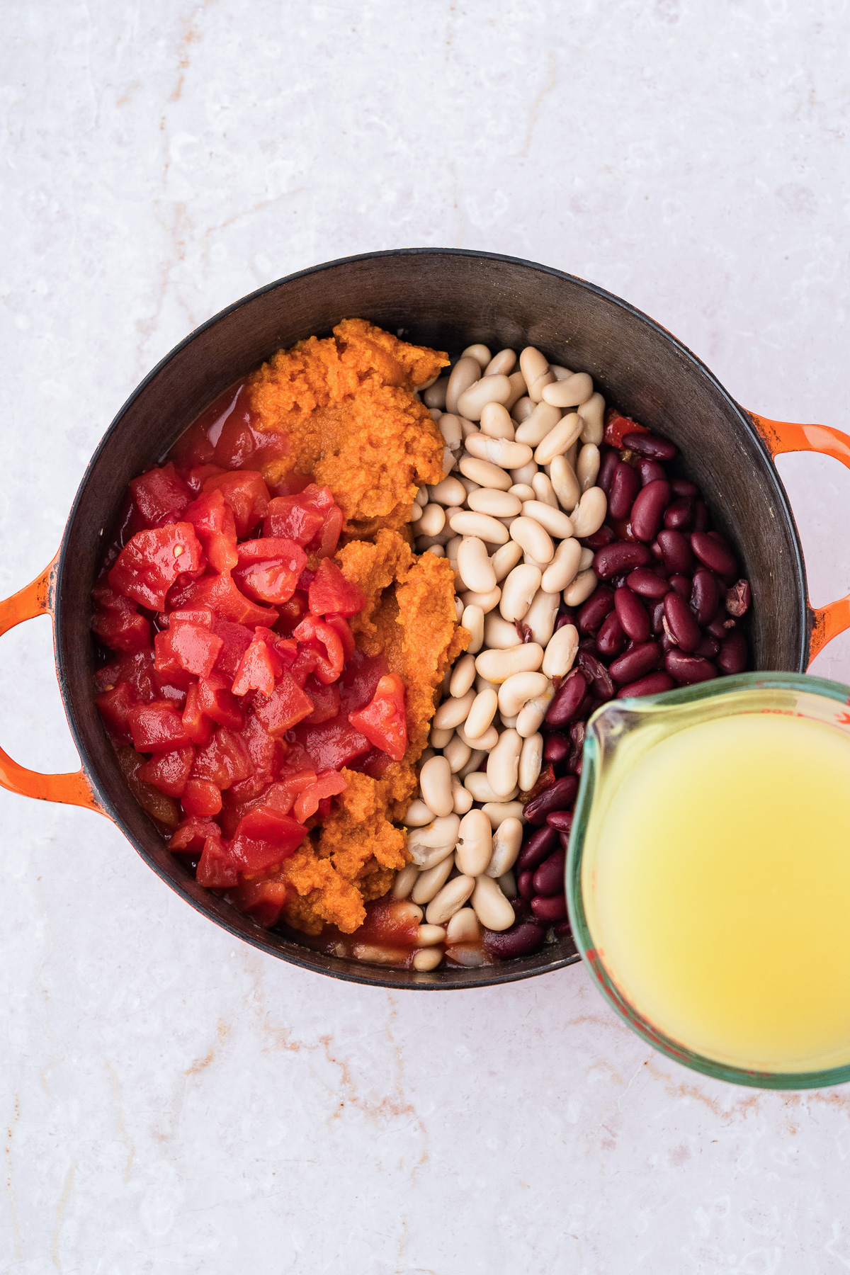 A pot containing leftover turkey pumpkin chili ingredients, including beans, tomatoes, and a measuring cup of broth.